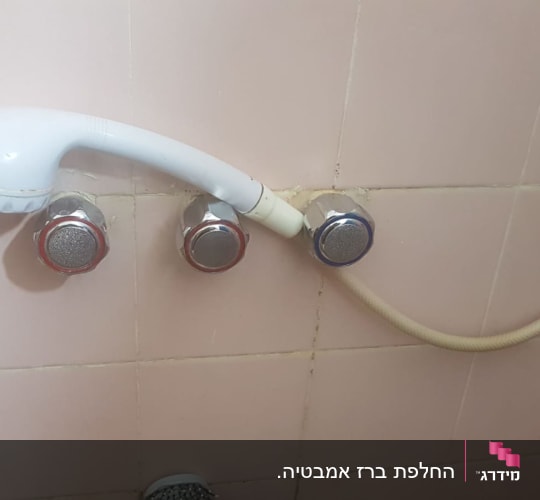 ראש מקלחת לבן עם ברזים על קיר קרמיקה